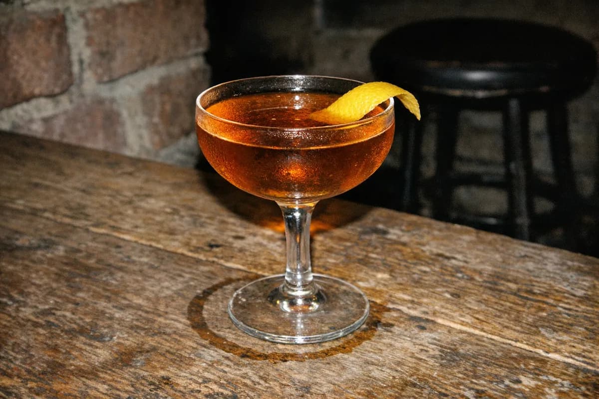 Close-up of a single coupe cocktail with lemon twist on a worn timber table at Waltz in Shoreditch, no people.